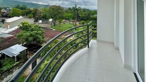 A balcony with a curved railing, a tiled floor, and a view of a residential area with houses and trees.