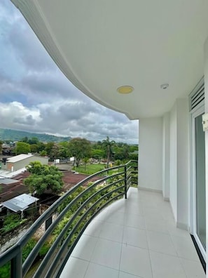 Un balcón con barandilla curva, piso de baldosas y vistas a un área residencial con casas y árboles.