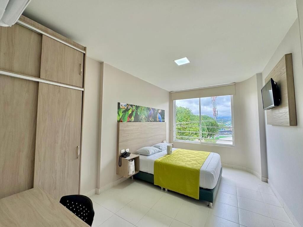 A hotel room with a bed, a desk, a wardrobe, a window with a view, and a mounted television.