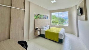 Ein Hotelzimmer mit Bett, Schreibtisch, Kleiderschrank, einem Fenster mit Aussicht und einem Wandfernseher.