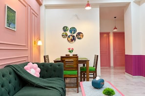 A cozy living room with a green sofa, a dining table with chairs, and a wall decorated with circular art pieces.