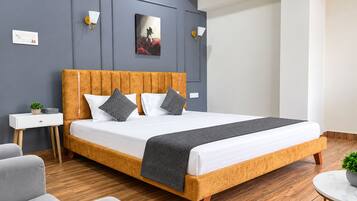 Un dormitorio moderno con cabecera de madera, una cama grande con ropa de cama blanca, dos mesitas de noche con lámparas y una mesita redonda con una planta.