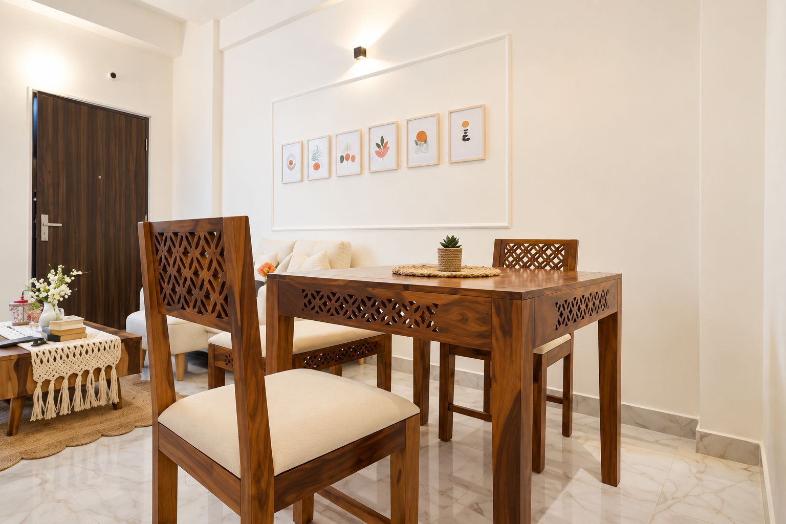 A dining area with a wooden table and chairs, a white wall with framed artwork, and a door in the background.
