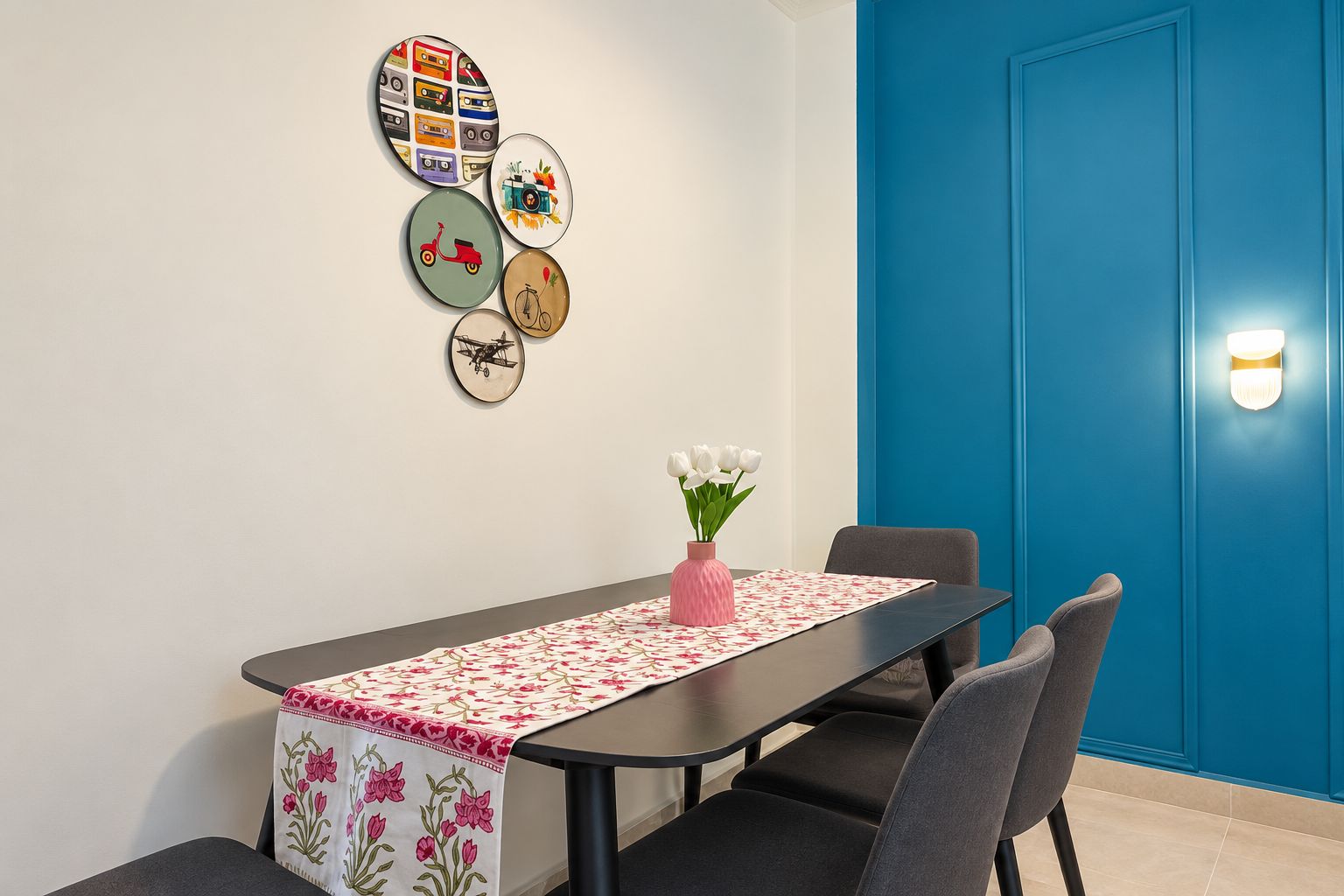 A dining area with a table set for two, a vase with flowers, and wall art.