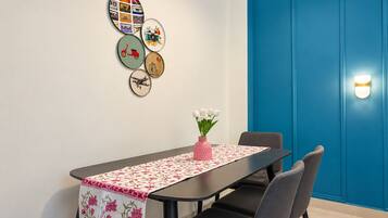 A dining area with a table set for two, a vase with flowers, and wall art.
