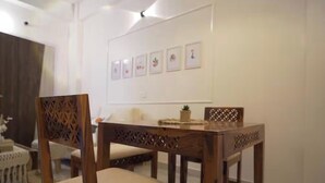 A dining area with a wooden table and chairs, a white wall with framed pictures, and a small potted plant on the table. - Beau Monde Suites (Guwahati)