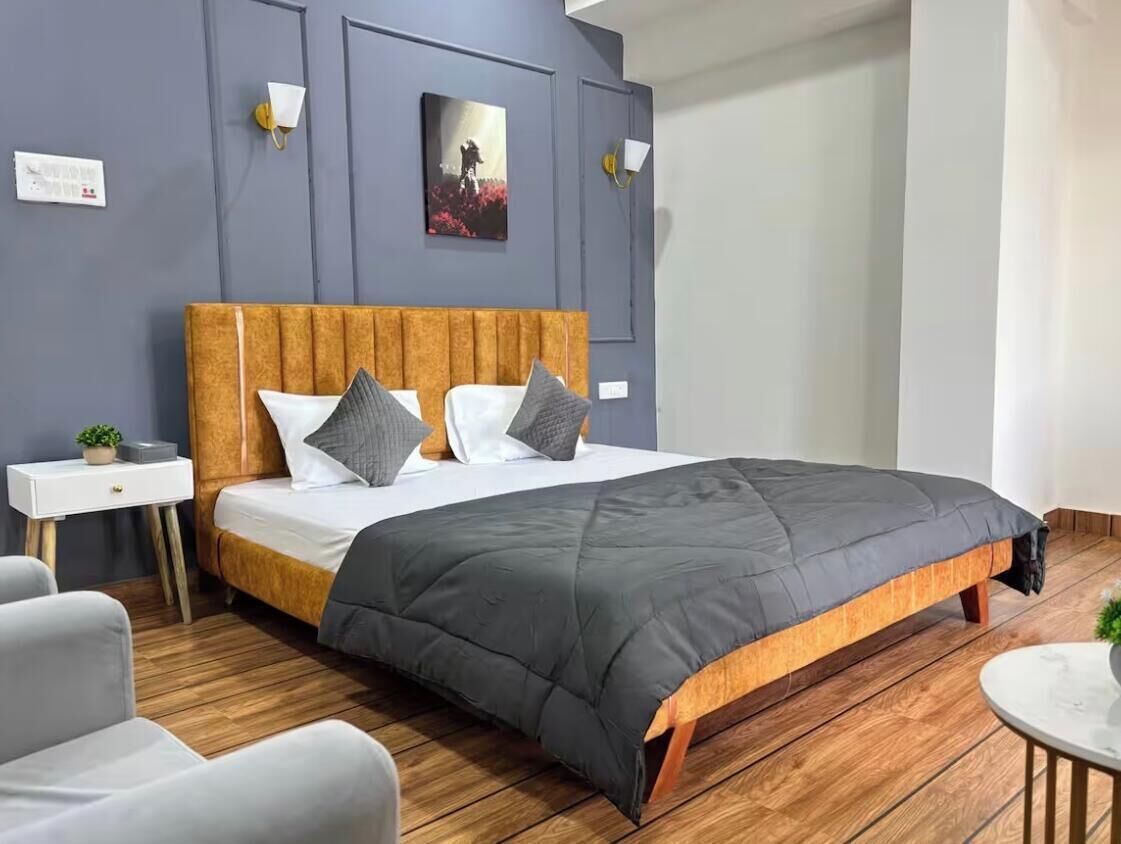 Ein modernes Schlafzimmer mit einem hölzernen Kopfteil, einer grauen Tagesdecke und einem Nachttisch mit einer Pflanze.