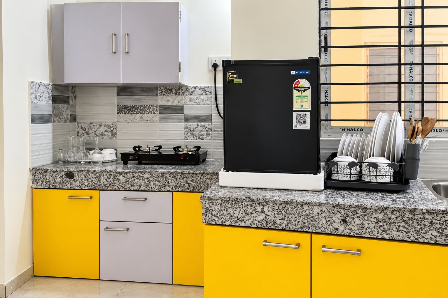 Una cocina con un refrigerador negro, encimera de granito y gabinetes amarillos.