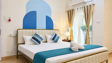 A hotel room with a bed, a headboard, a bedside table with a lamp, a window with curtains, and an air conditioning unit.