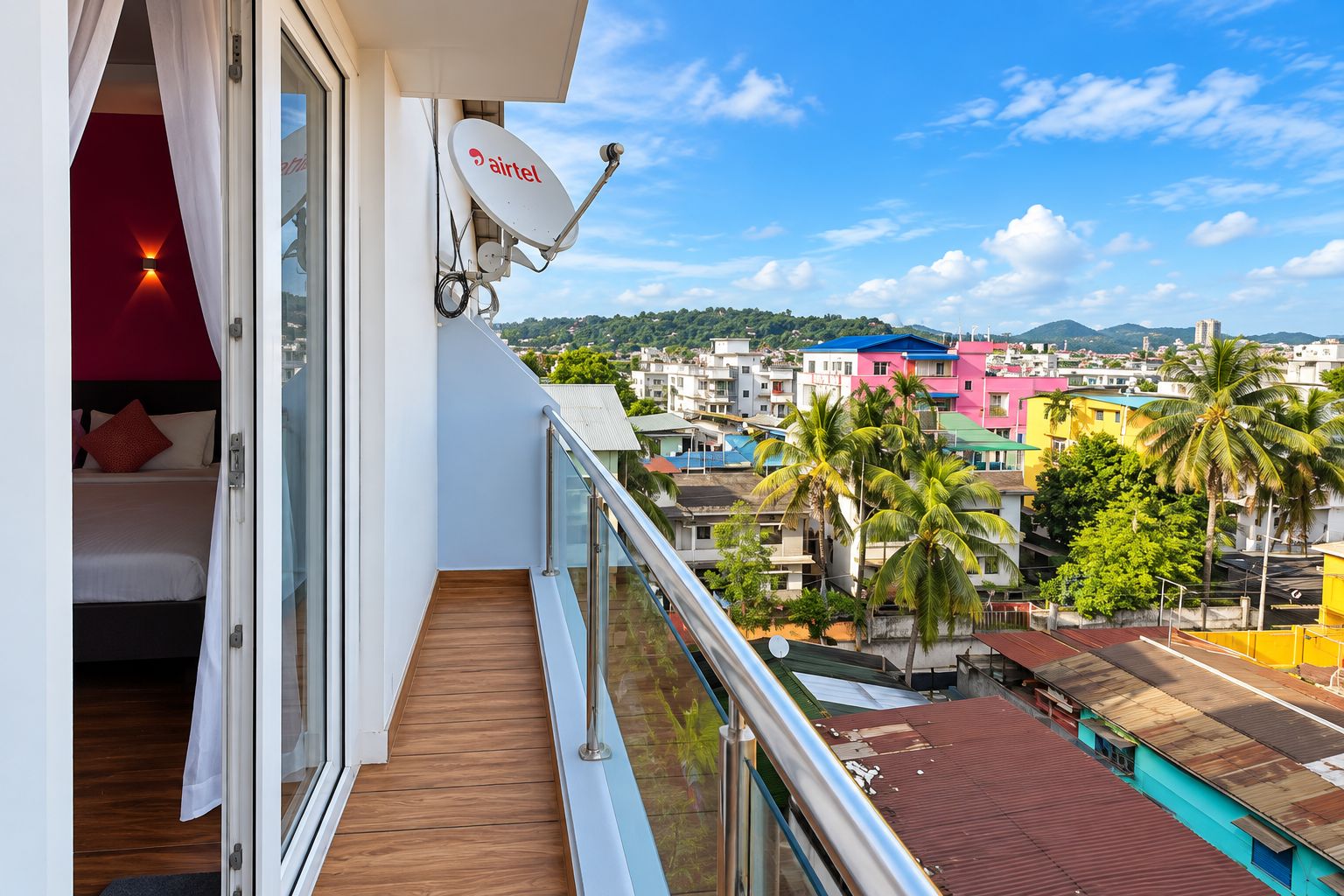 A balcony with a view of a cityscape, a satellite dish, and a bed with a red pillow.