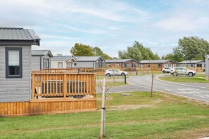 A row of single-story mobile homes with attached garages, a grassy area, and a paved road. - Host & Stay | Wilderness Wood Lodge (Pickering)