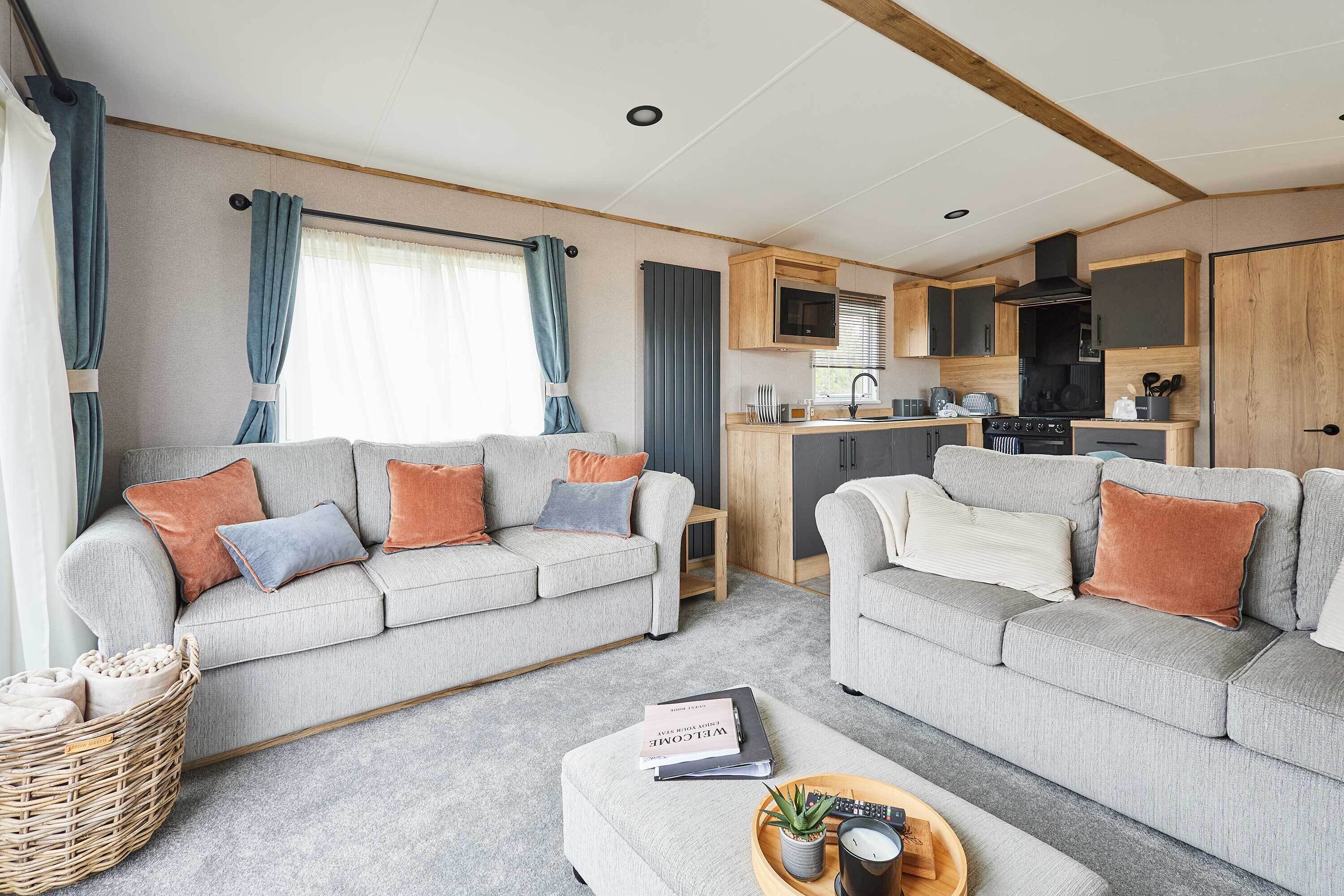 A modern living room with two sofas, a small table, and a kitchen area with wooden cabinets and appliances.