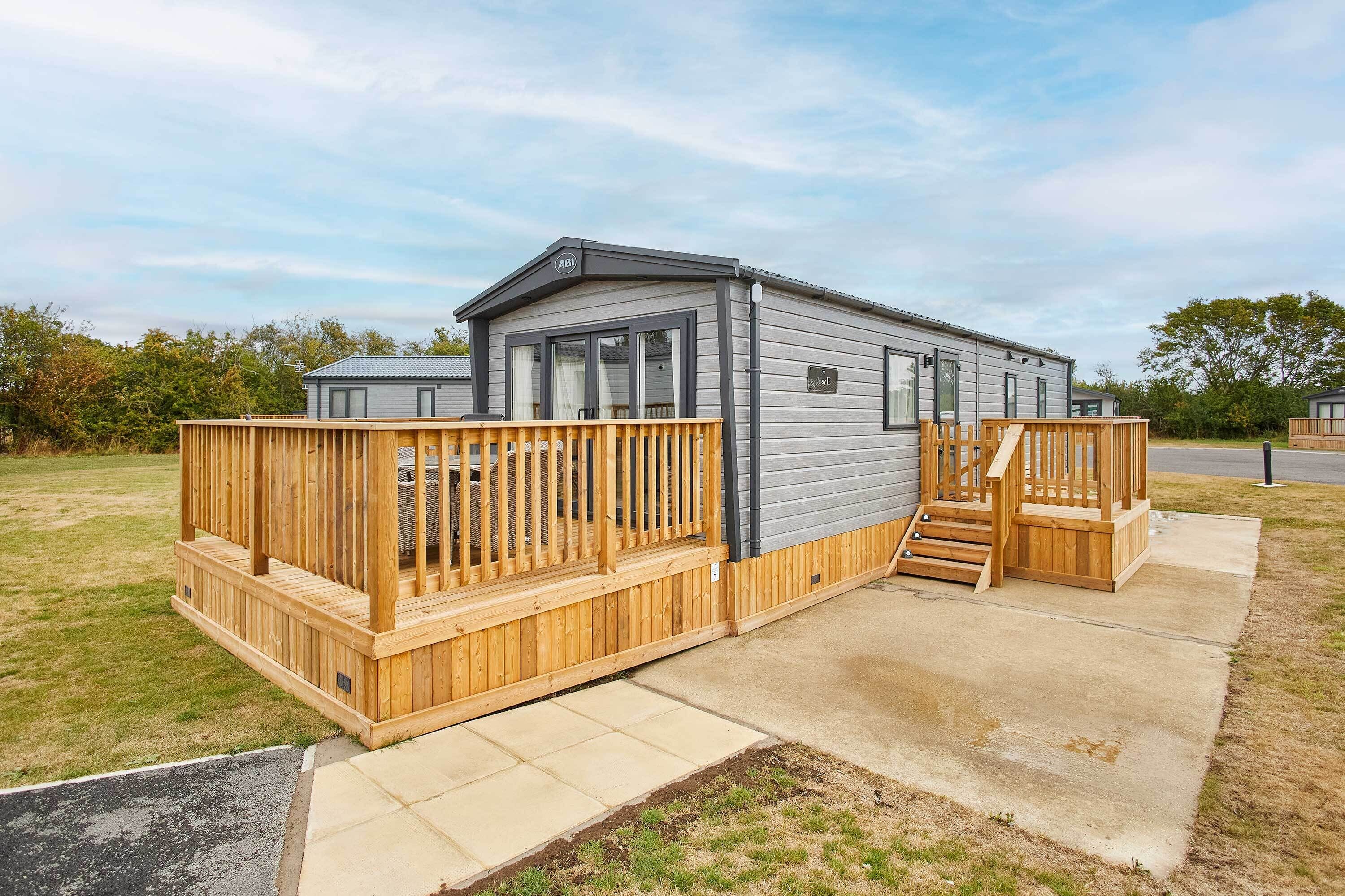 A mobile home with a wooden deck, a small porch, and a concrete pathway leading to the entrance.