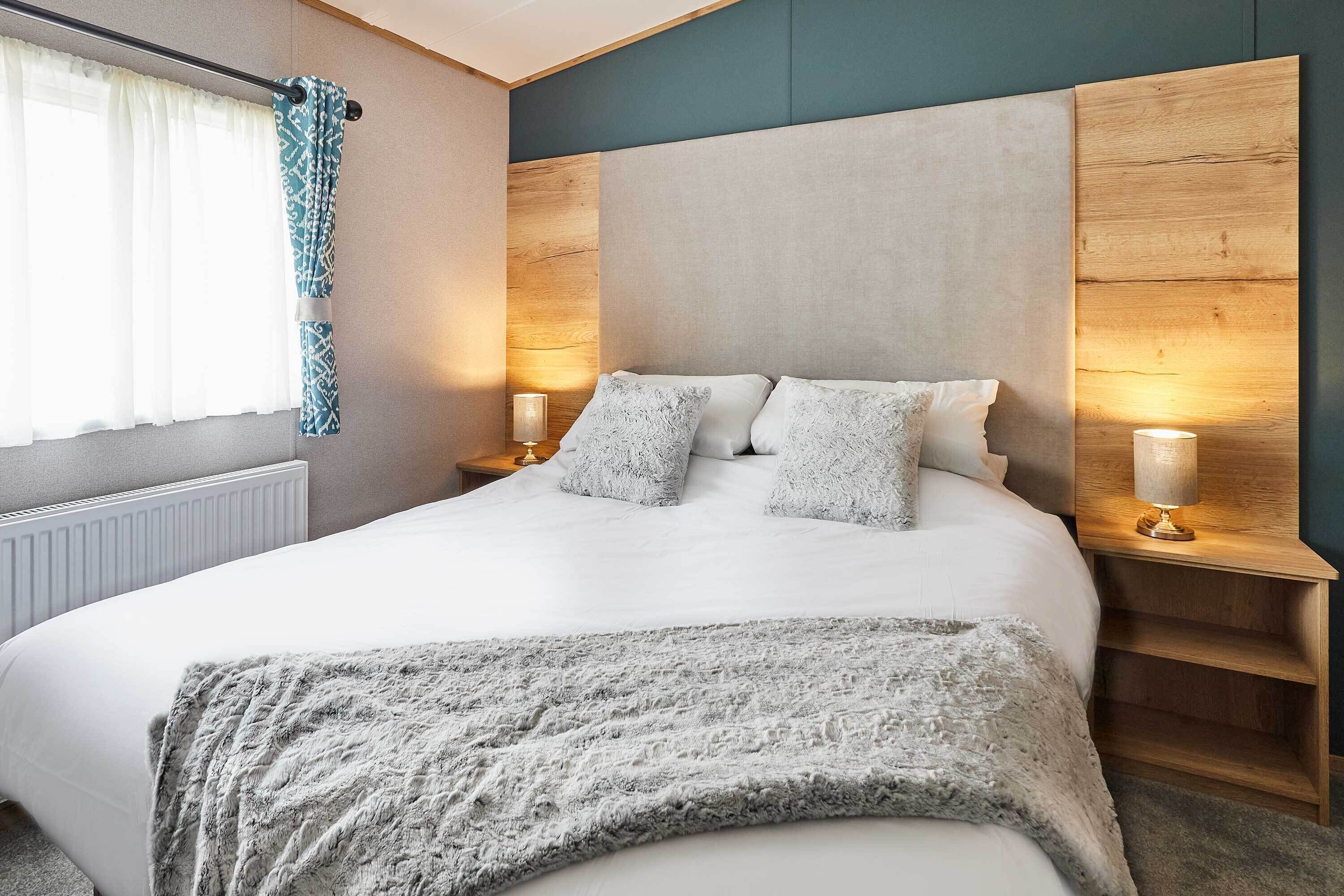 A modern bedroom with a large bed, two bedside tables with lamps, a window with curtains, and a radiator.