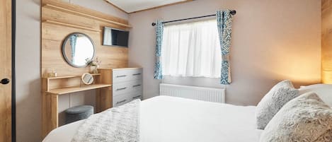 Une chambre à coucher avec un lit, une commode, un miroir, un téléviseur et une fenêtre avec des rideaux.