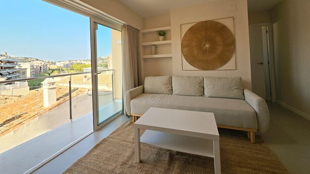 A modern living room with a sofa, a coffee table, and a large window offering a city view.