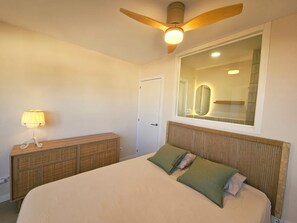 Une chambre à coucher avec un lit, une lampe de chevet, un ventilateur de plafond, un miroir et une porte.