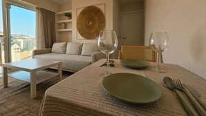 A hotel room with a bed, a sofa, a dining table with a plate, cutlery, and wine glasses.