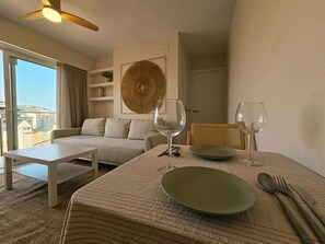 A hotel room with a bed, a sofa, a dining table with a plate, cutlery, and wine glasses.