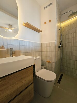 A modern bathroom with a white sink, toilet, and shower area. - ‘Ocean View’ Apartment with Sea Views, Balcony, and Wi-Fi (Sant Feliu de Guíxols)