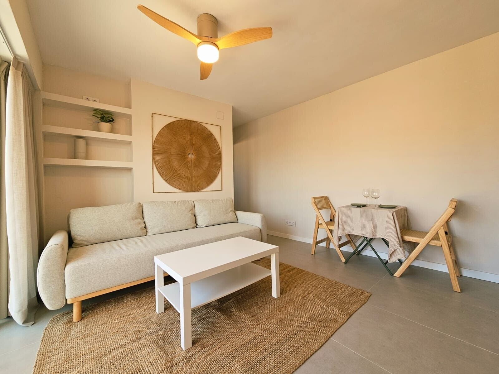 Un soggiorno con divano, tavolino, tavolo da pranzo con sedie, ventilatore a soffitto e un'ampia decorazione a parete.