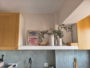 A kitchen with wooden cabinets, a tiled backsplash, a framed fish illustration, and a potted plant.