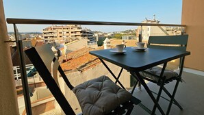 Ein Balkon mit Tisch und Stühlen, der auf einen Stadtblick mit Gebäuden und blauem Himmel blickt.
