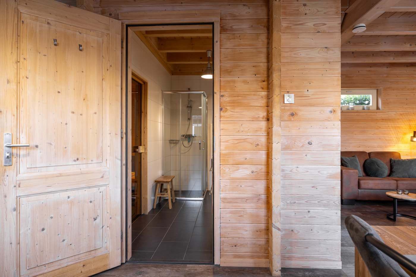 A wooden interior with a wooden door, a shower area, and a seating area with a sofa and table.