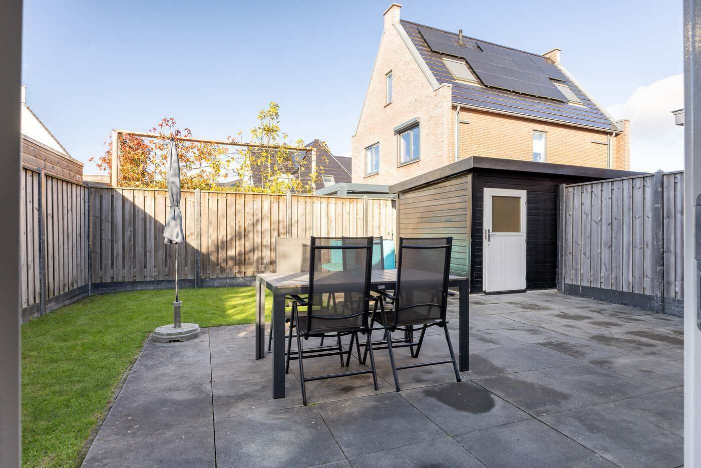 A patio with a table and chairs, a wooden fence, and a house with solar panels.