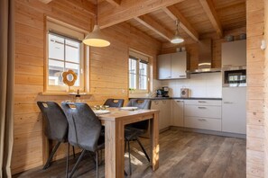 A wooden interior with a dining table, chairs, a kitchen area, and a window with a decorative wreath. - Holiday home with sauna in Oostkapelle | Zeeduinsepoort 14a (Oostkapelle)