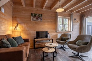 A cozy wooden interior with a sofa, armchairs, a TV, and a small table. - Holiday home with sauna in Oostkapelle | Zeeduinsepoort 14a (Oostkapelle)