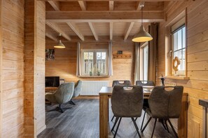 A wooden interior with a dining table, chairs, pendant lights, a radiator, and a window with curtains. - Holiday home with sauna in Oostkapelle | Zeeduinsepoort 14a (Oostkapelle)