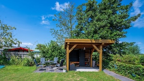 Un belvédère en bois, avec une table et des chaises, entouré d’une pelouse et d’arbres.