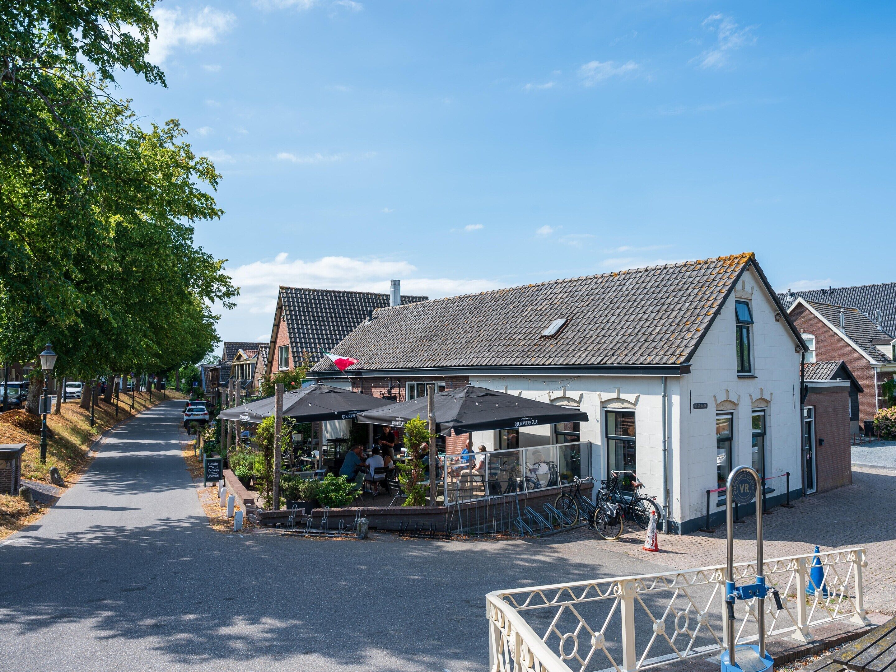 Straßenansicht mit einem Café, Fahrrädern und einem weißen Gebäude mit einem Ziegeldach.