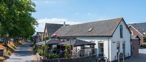 Straßenansicht mit einem Café, Fahrrädern und einem weißen Gebäude mit einem Ziegeldach.