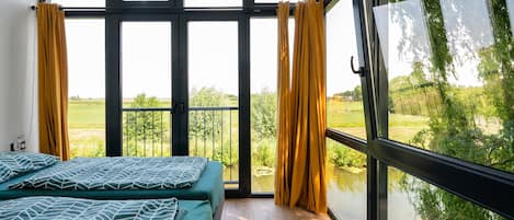 A room with two beds, large windows, and a view of a green landscape.