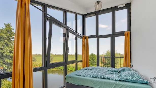 Une chambre avec une grande fenêtre, un lit avec une literie verte et une vue sur un paysage verdoyant.