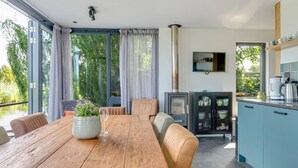 Une cuisine moderne dotée d’une cuisinière intégrée, d’un coin repas avec une table et des chaises en bois, et offrant une vue sur la verdure grâce à de grandes fenêtres.