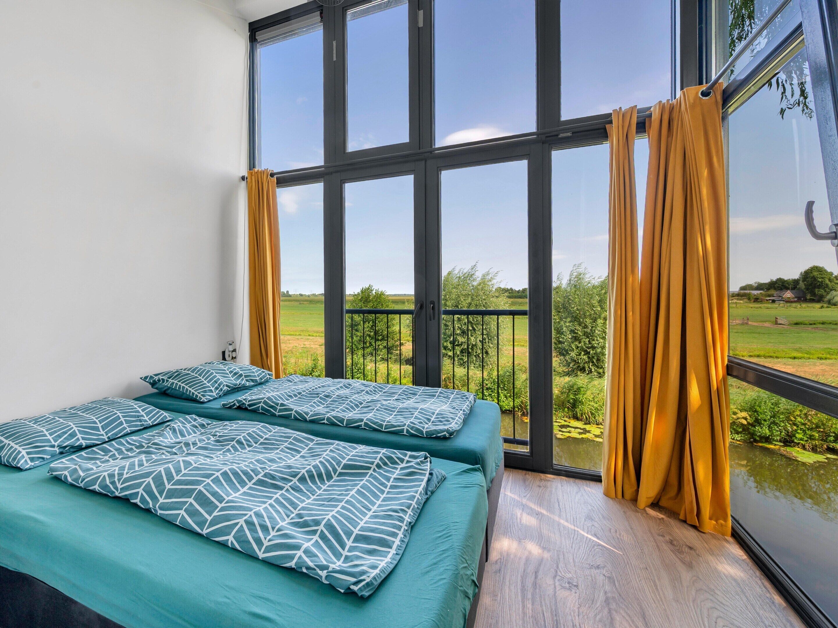 Una habitación con un ventanal grande, una cama con ropa de cama estampada y vistas a un paisaje verde.