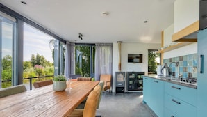 Une cuisine moderne avec une table et des chaises en bois, une cuisinière encastrée et une vue sur la verdure à l’extérieur.