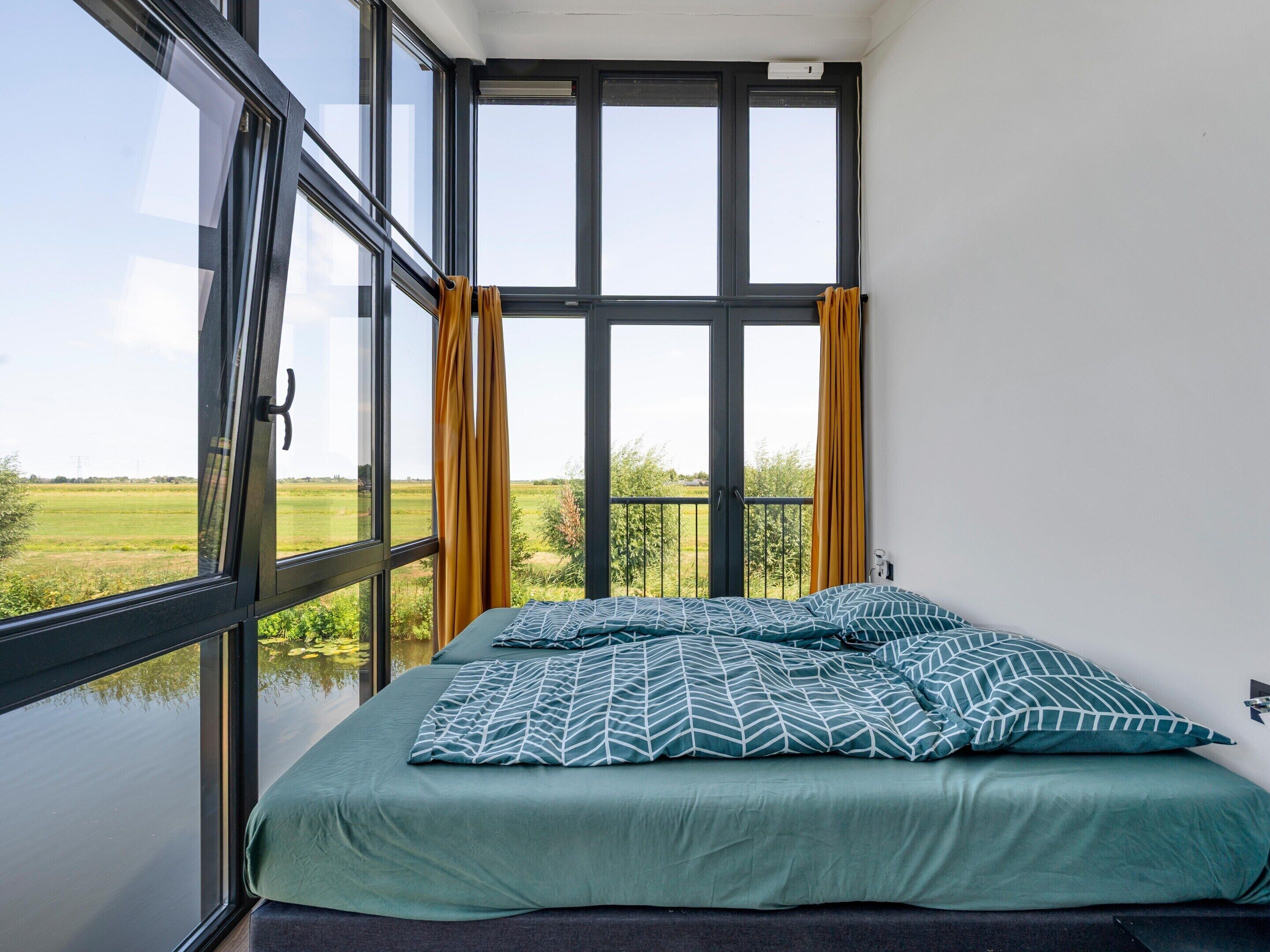 A bedroom with a large window, a bed with patterned bedding, and curtains.