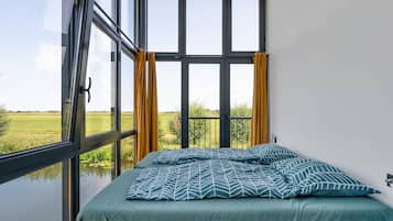 Een slaapkamer met een groot raam, een bed met beddengoed met een patroon, en gordijnen.