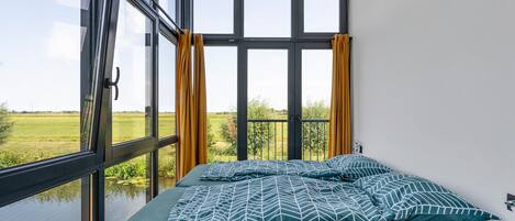 A bedroom with a large window, a bed with patterned bedding, and curtains.