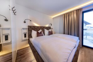 A modern hotel room with a large bed, a bedside table, a built-in shelf, and a view of the outdoors. - Penthouse with a dream view (Bramberg am Wildkogel)