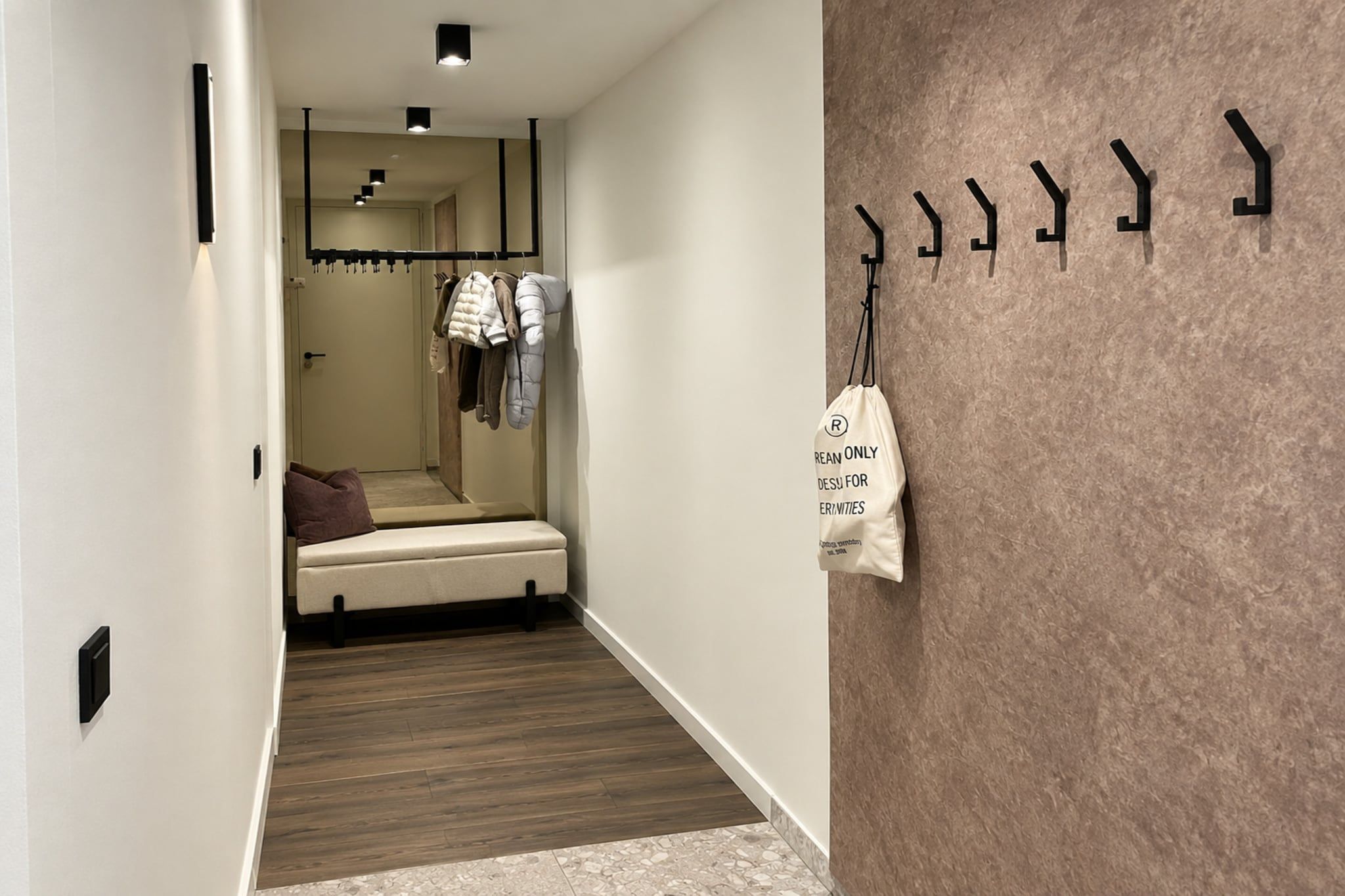 A hallway with a bed, a coat rack, and a wall-mounted bag rack.