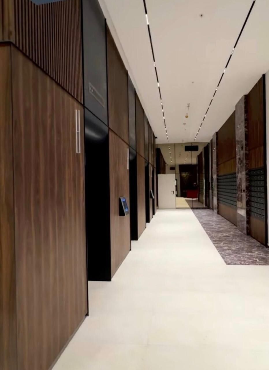 A corridor with a modern design, featuring a combination of wooden paneling and glass doors, leading to a room with a red carpet.