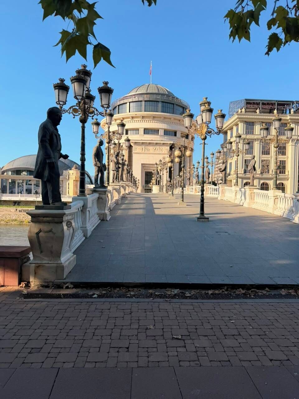 Ein gepflasterter Weg mit einer Statue und verzierten Straßenlaternen, der zu einem großen Gebäude mit einer Kuppel führt.