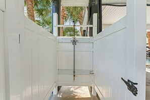 A narrow passageway with a metal gate, white walls, and a view of palm trees outside. - Sunshine Daydream - Close to Beach/Shared Pool (North Myrtle Beach)