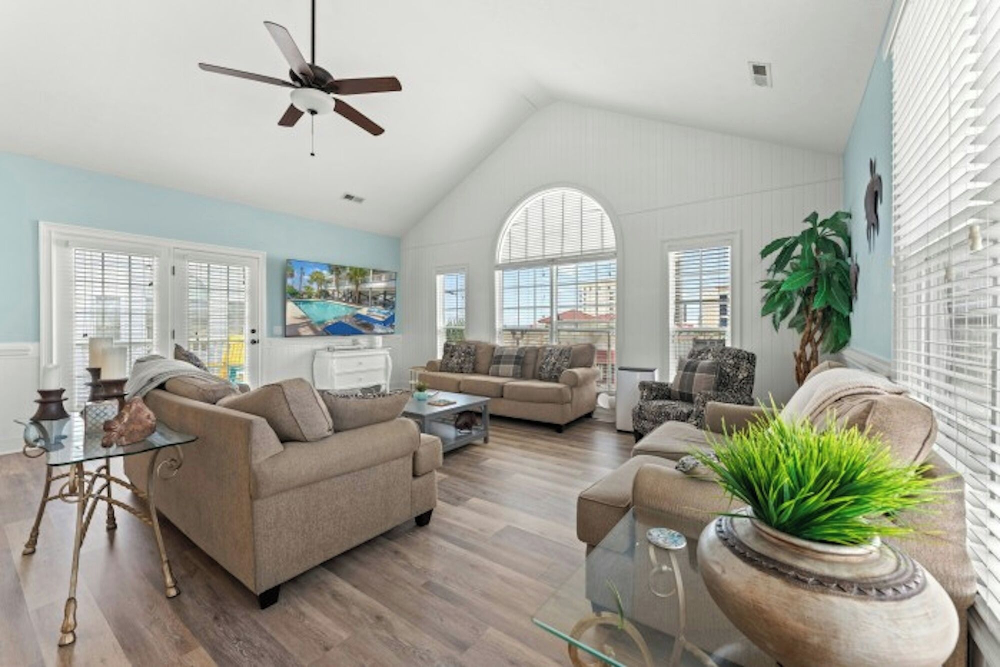 A spacious living room with a high ceiling, large windows, and a ceiling fan.