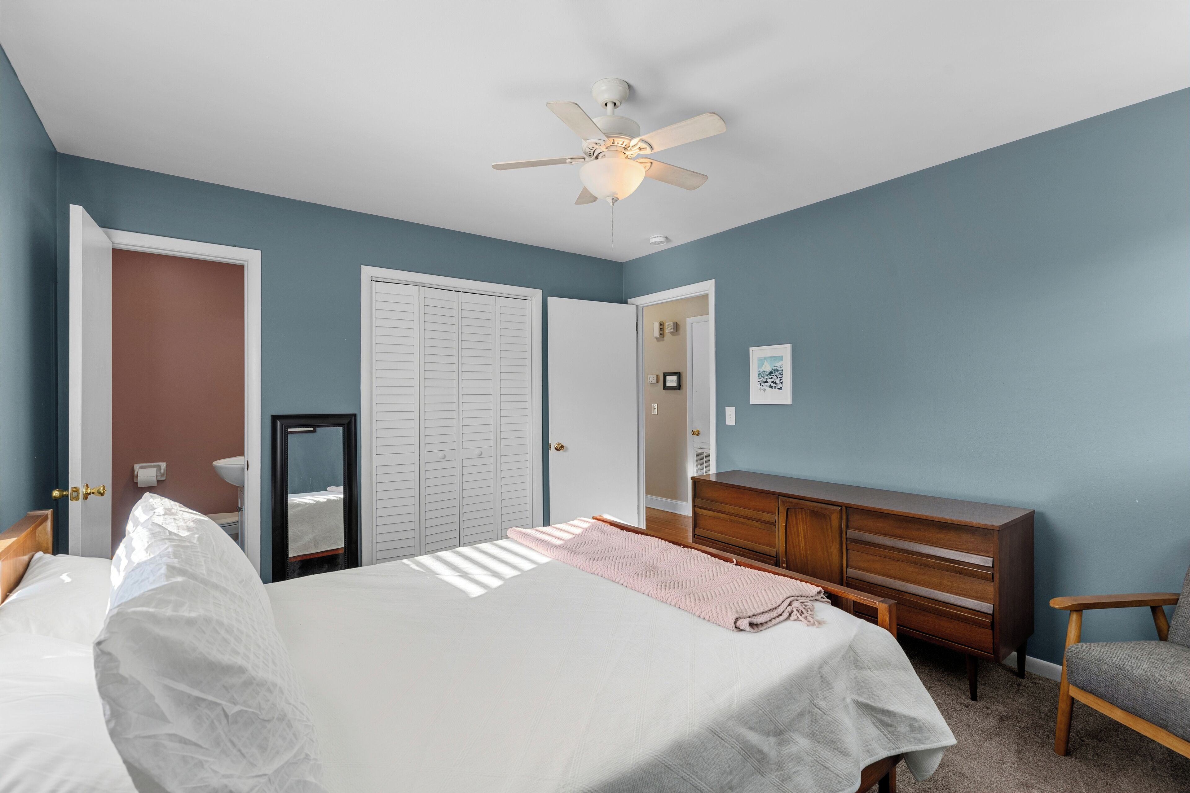 A bedroom with a bed, dresser, mirror, and a ceiling fan.
